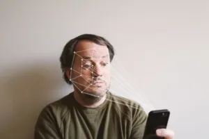 HOMEM COM ROSTO MAPEADO UTILIZANDO UM CELULAR, DEMONSTRANDO TECNOLOGIA DE RECONHECIMENTO FACIAL.