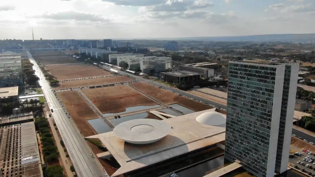 Vista aérea do eixo monumental de Brasília, mostrando os principais edifícios governamentais como o Congresso Nacional e o Palácio da Alvorada. A imagem captura a modernidade e a arquitetura característica da capital do Brasil.