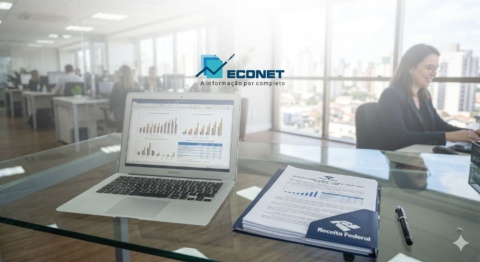 Ambiente de escritório moderno com laptop exibindo gráficos, documentos e receitafederal na mesa, com pessoas ao fundo trabalhando em ambiente corporativo.